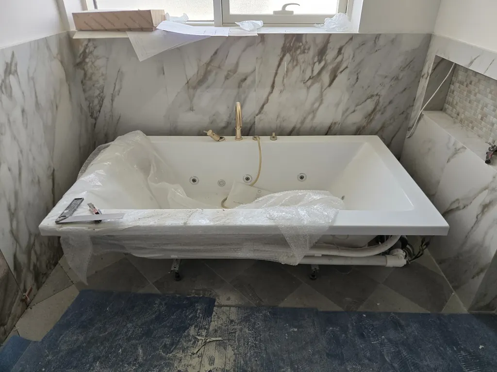 A whirlpool bath set into marble-look walls before the glass and fittings
