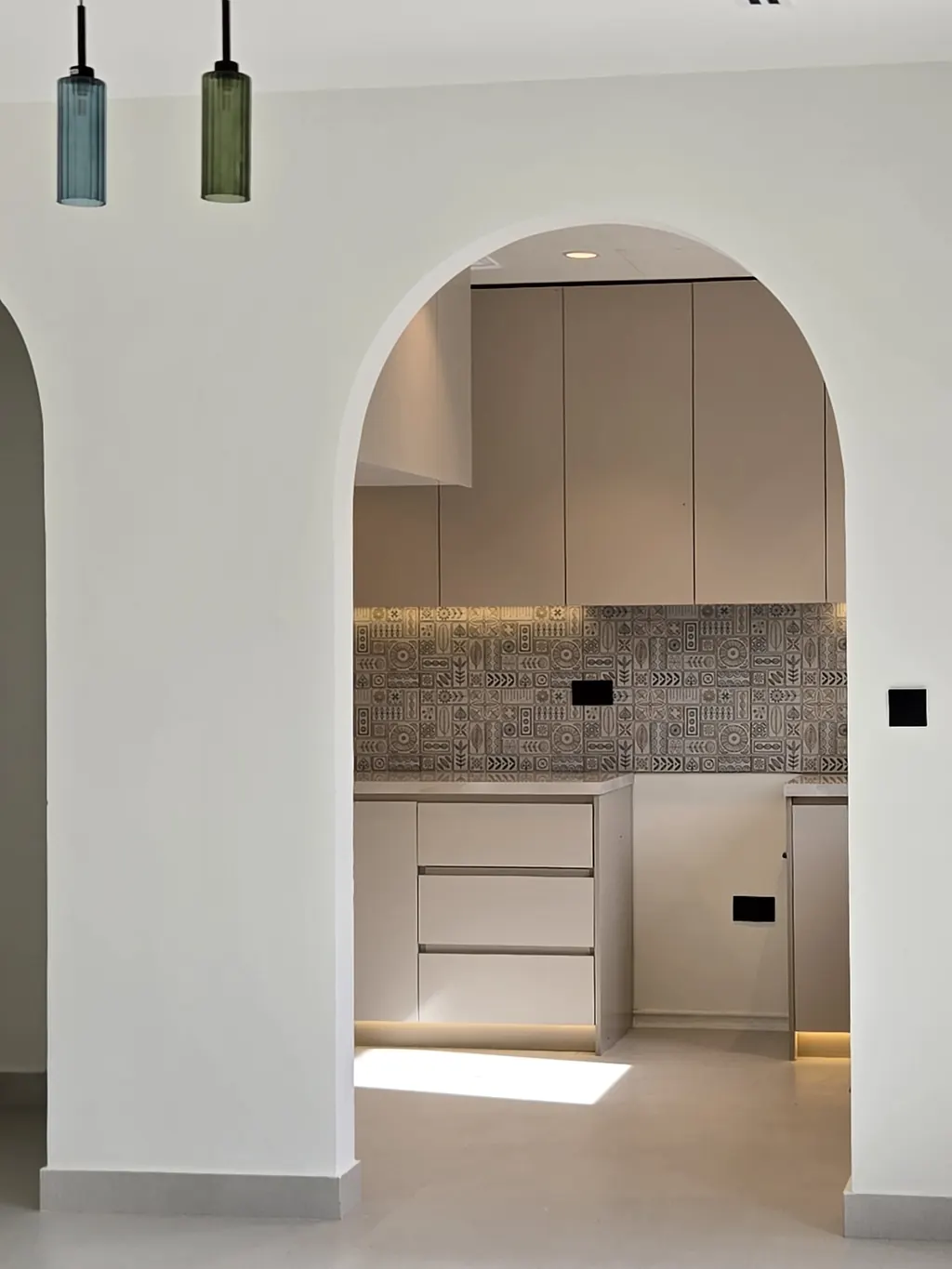 Kitchen seen through an arched opening with pendant lights