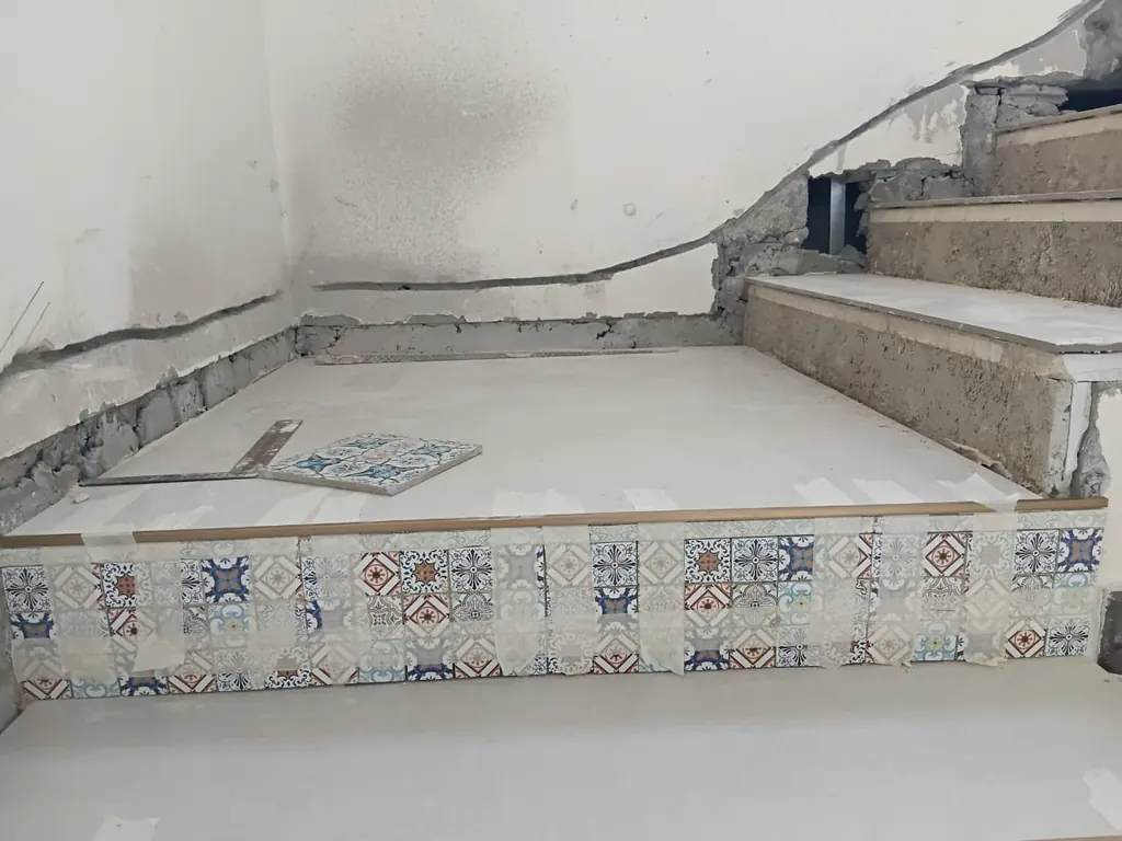 Patterned tile risers being set on the bottom steps of the staircase